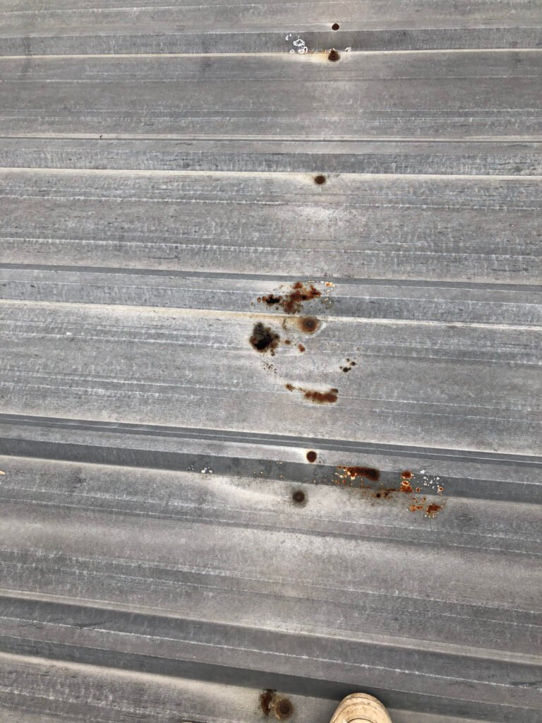 Close-up of corrosion and deteriorated fasteners on an aging commercial metal roof before restoration