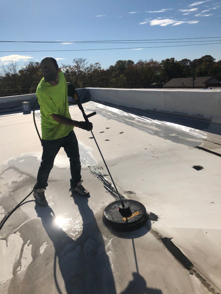Commercial roofing contractor pressure cleaning an existing roof during preparation for a roof restoration system