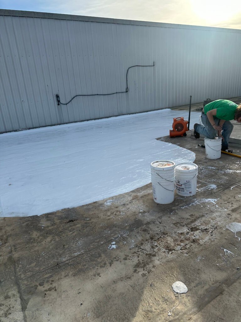 Commercial roofing contractor applying a white fluid-applied roof coating system during restoration