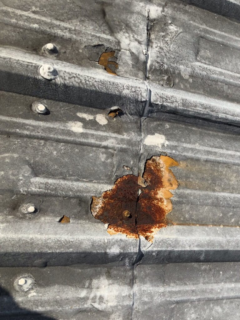Severe corrosion and rust deterioration at a seam on an aging commercial metal roof before restoration