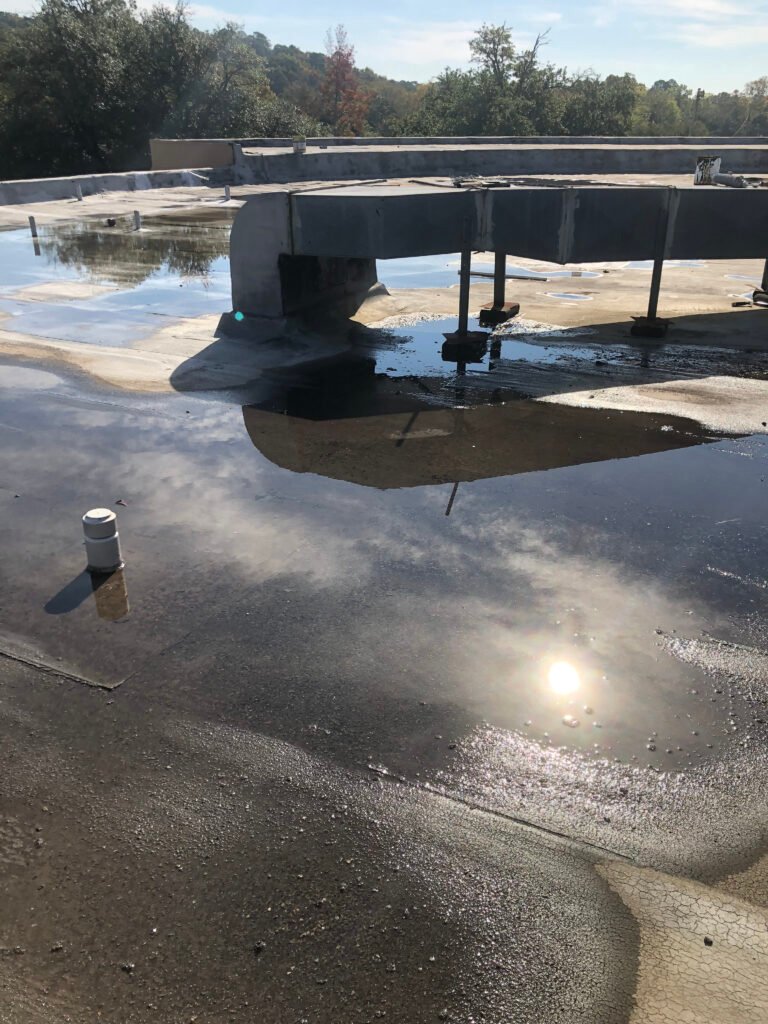 Ponding water across an aging commercial flat roof around rooftop HVAC equipment