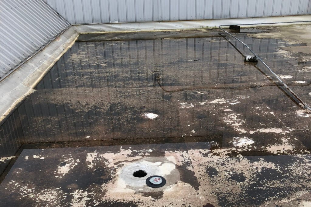 Severe ponding water surrounding a roof drain on an aging commercial flat roof